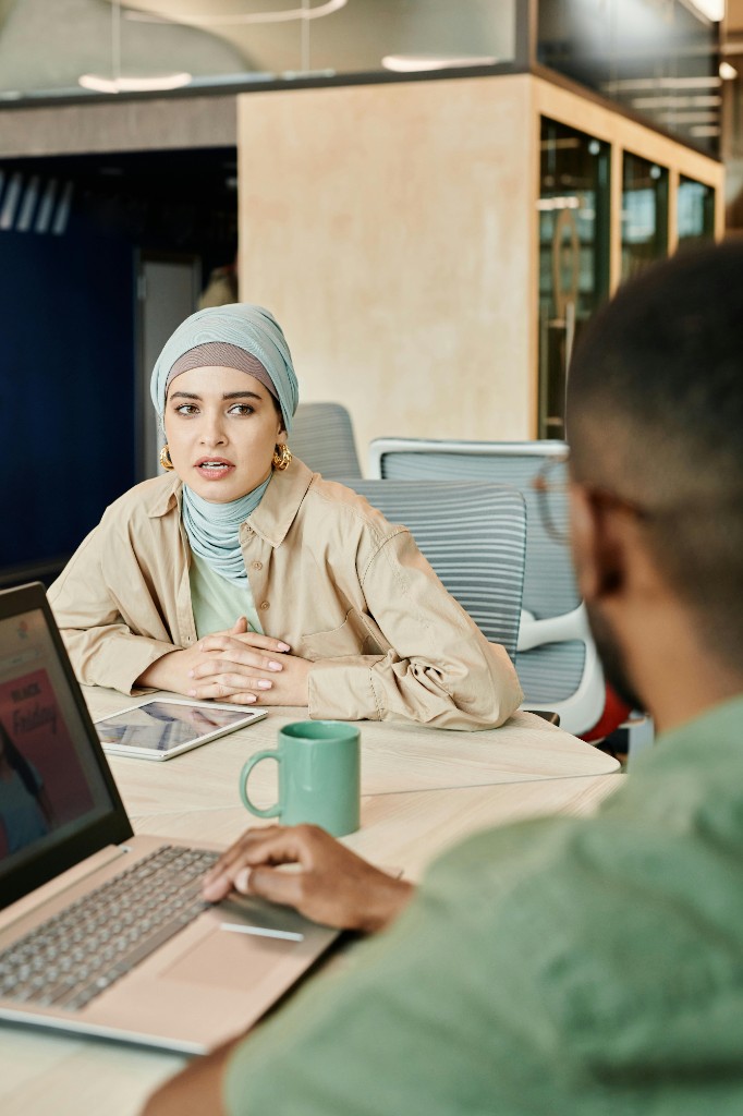 A professional in a light blue hijab seated at a conference table in discussion; bright contemporary office.